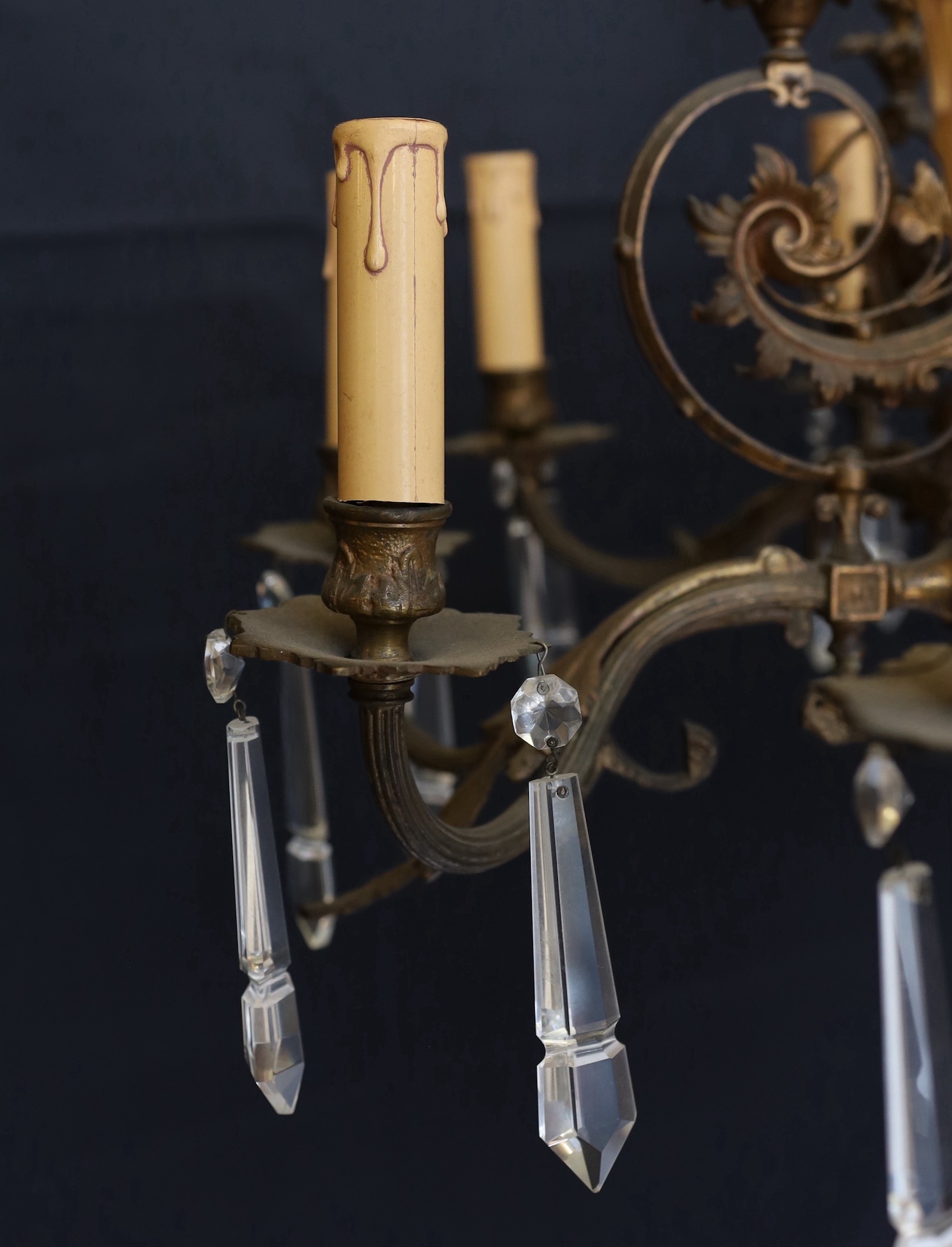 A Victorian bronze ten light gasolier with ornate scrolling foliate frieze and central ceramic stem, hung with spear shaped drops, later fitted for electricity, height 92cm. width 60cm